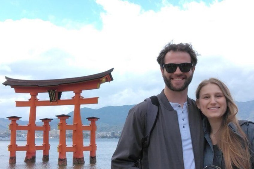 Een koppel staat voor een traditionele Japanse torii-poort aan een waterpartij, met bergen op de achtergrond. 1