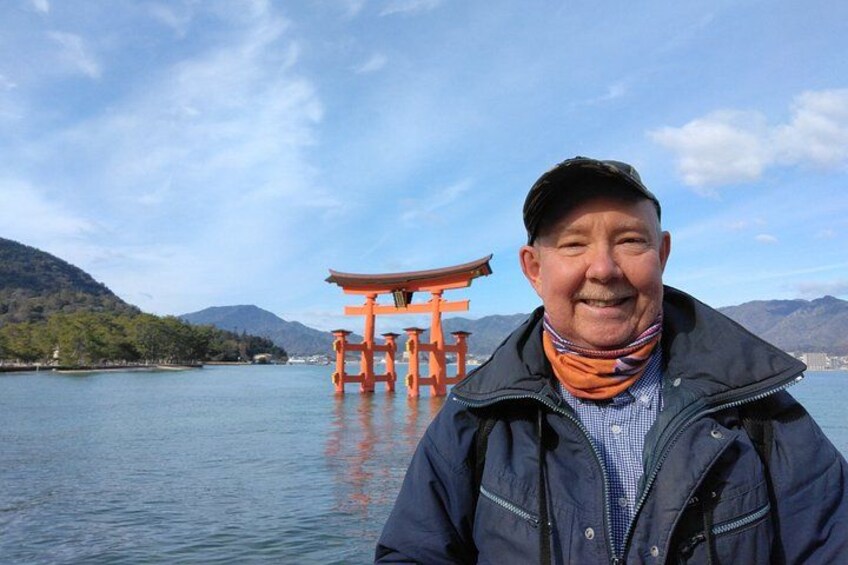 Una persona in piedi di fronte a un tradizionale torii giapponese, vicino all'acqua, con montagne sullo sfondo. 2