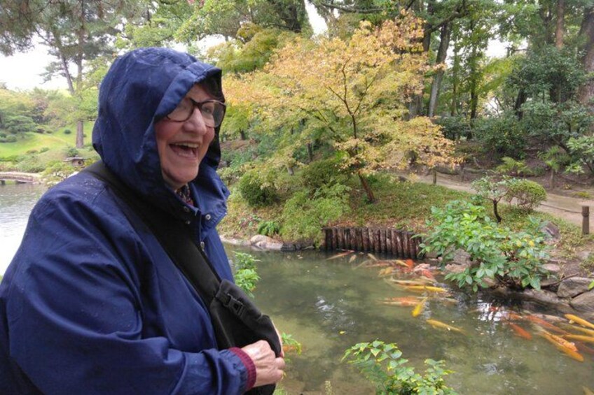 En person i en blå regnjacka står vid en damm med koi-fiskar. 3