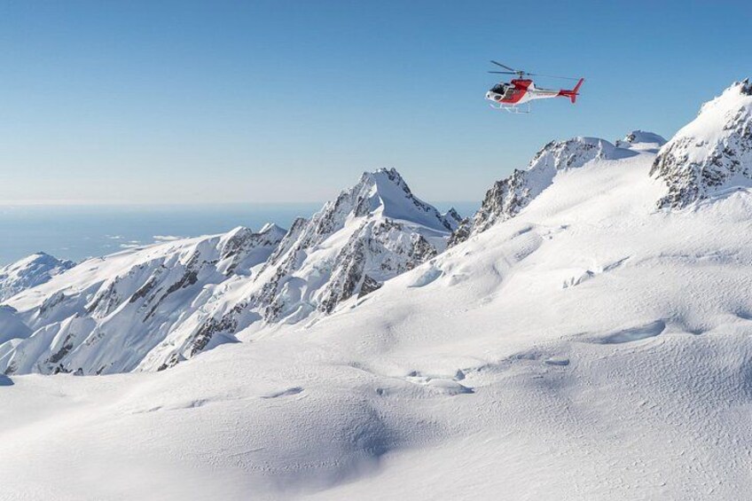 Ein Hubschrauber überfliegt ein schneebedecktes Gebirge. 3