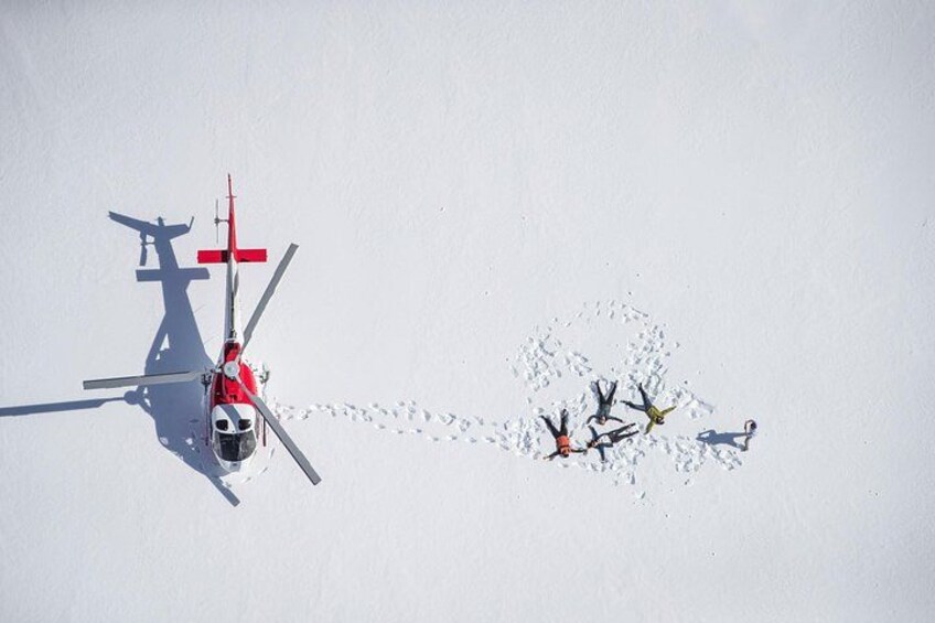 Ein Hubschrauber in Rot-Weiß, eine Person mit roter Jacke und eine Gruppe Menschen im Schnee. 4