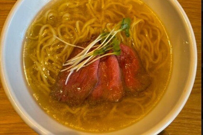 Un tazón de ramen con fideos, una porción de carne y una guarnición. 4