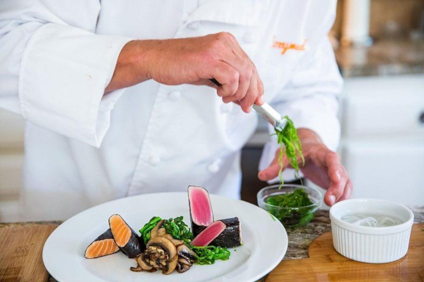 A chef preparing a dish with salmon, mushrooms, and greens on a white plate. 1