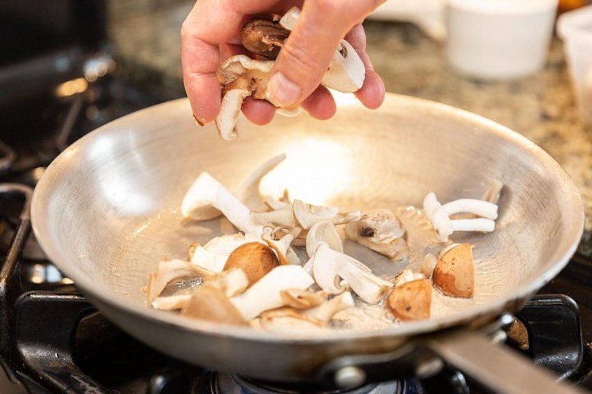 A hand adding sliced mushrooms to a frying pan on a stove. 2