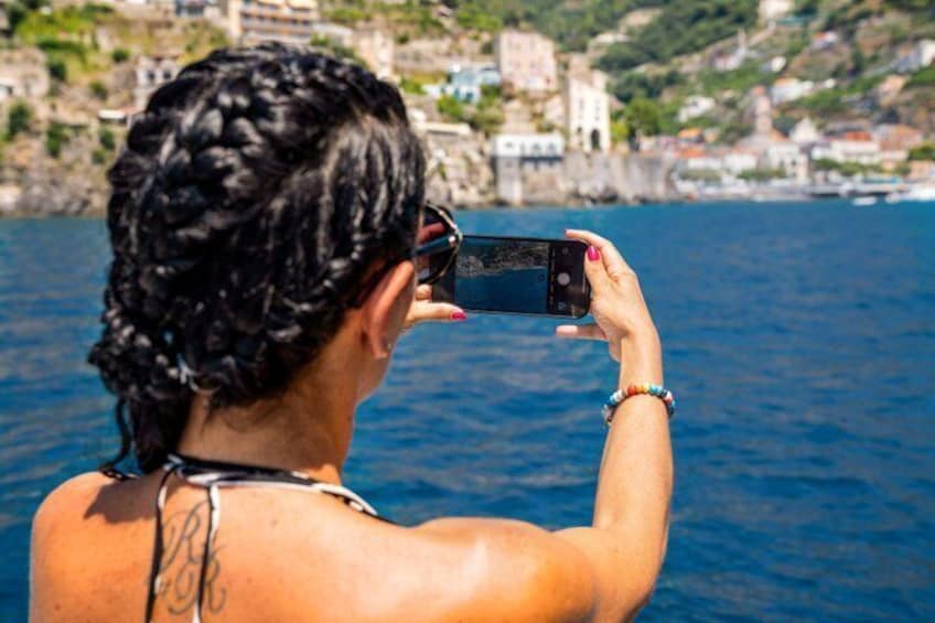 Una persona tomando una fotografía con un teléfono inteligente cerca de un cuerpo de agua, con edificios y colinas al fondo. 4