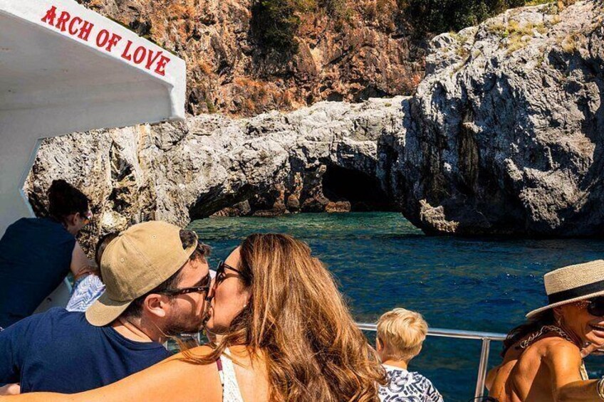 Un litoral rocoso con un bote identificado como 'ARCH OF LOVE' y gente disfrutando de la vista. 3