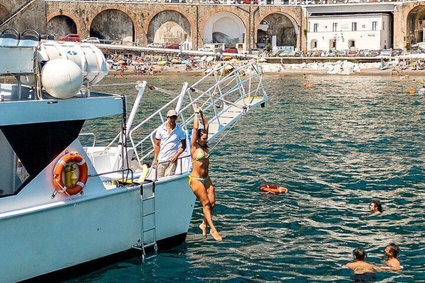 A woman in a bikini jumping off a boat into the water, with a lifebuoy and a ladder on the boat. 3