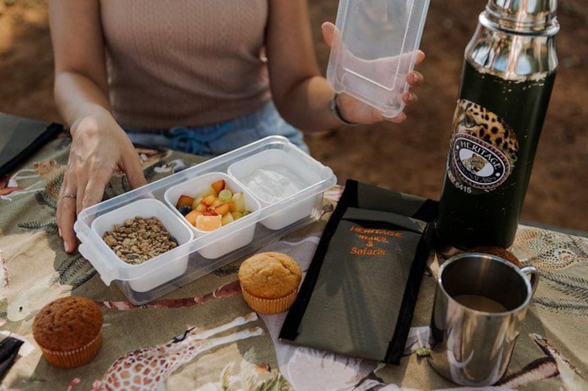 A meal setup with a container of snacks, a bottle, a muffin, and a packet of snacks on a table. 2