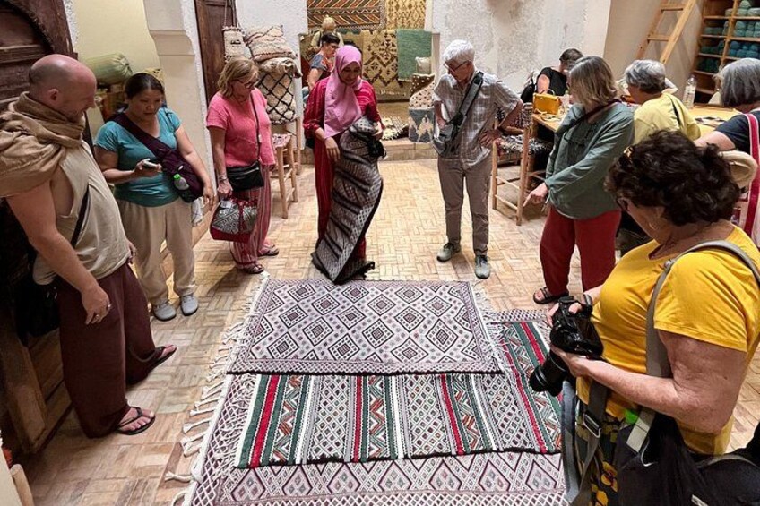 Een groep mensen verzameld rond een vloerkleed met een patroon in een kamer met houten vloeren en traditionele decoratie. 2