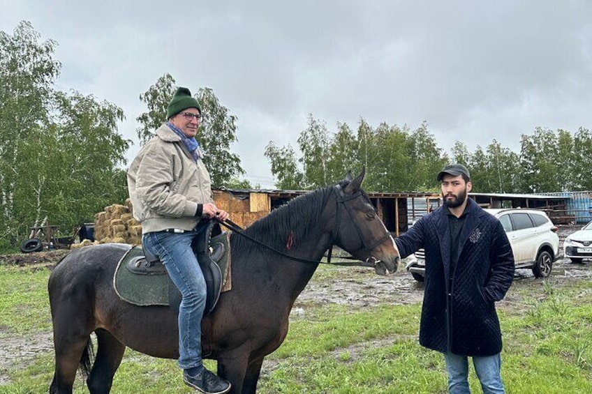Two people interacting with a horse in an outdoor setting with hay bales and vehicles in the background. 5