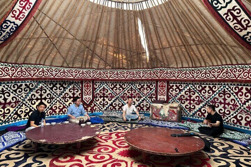 A traditional yurt with intricate patterns on the walls and a round table in the center. 1