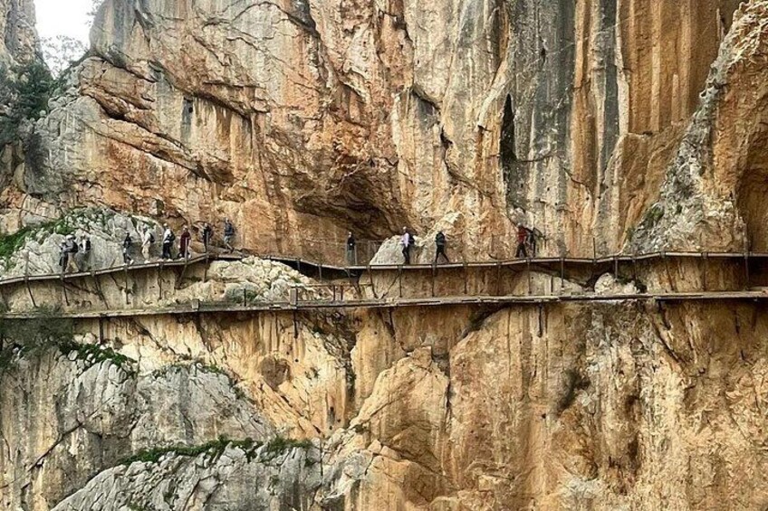 A narrow wooden bridge with people walking across it, surrounded by steep rocky cliffs. 2
