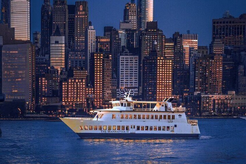 A white ferry named "The Manhattan II" on a body of water with a city skyline in the background. 1