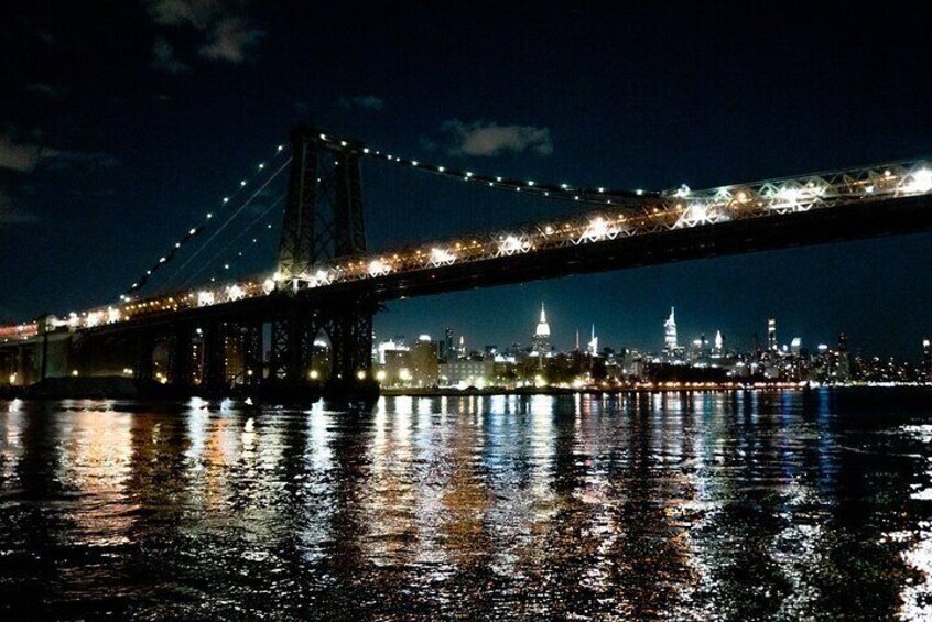 A nighttime view of a bridge with lights reflecting on the water, a city skyline with illuminated buildings, and a prominent tower structure. 2