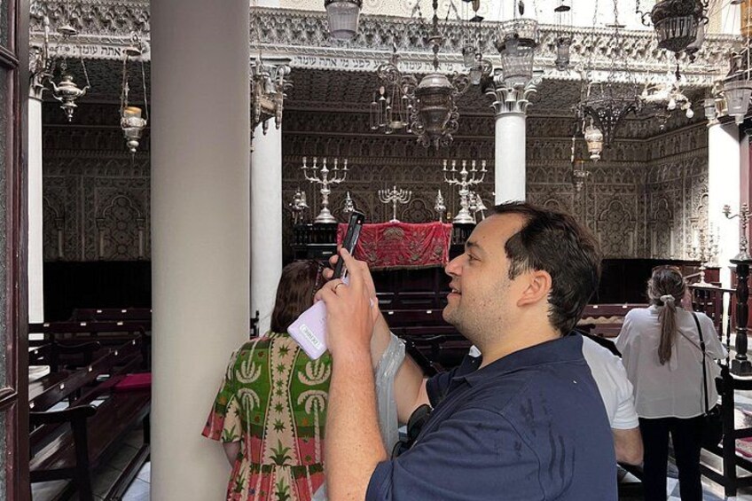 A person taking a photo inside a building with ornate decorations and a large chandelier. 2
