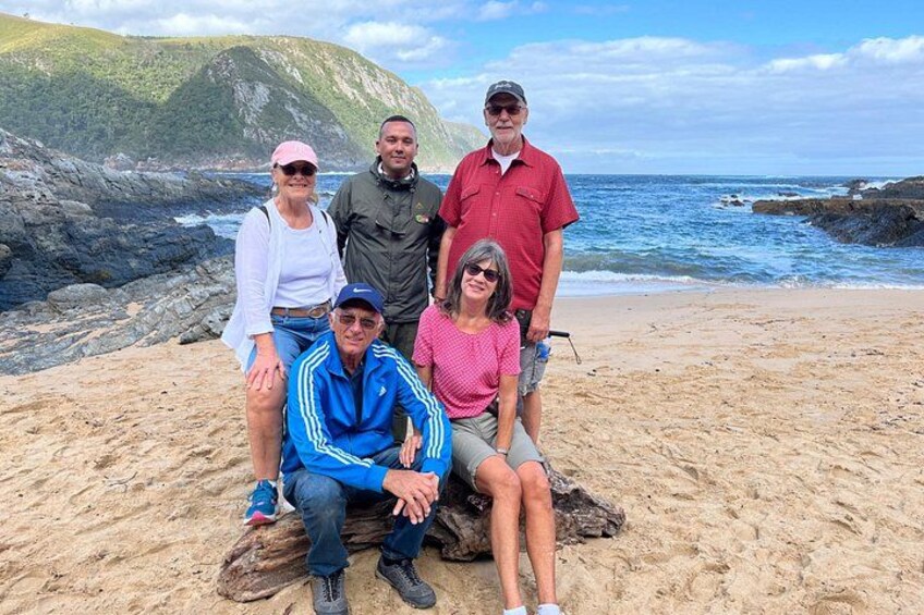 Eine Gruppe von Menschen an einem sandigen Strand mit felsigen Klippen und dem Meer im Hintergrund. 1