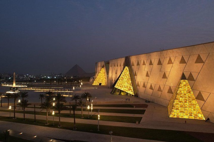 Un bâtiment moderne aux motifs triangulaires illuminés, avec une rivière et une pyramide en arrière-plan. 5