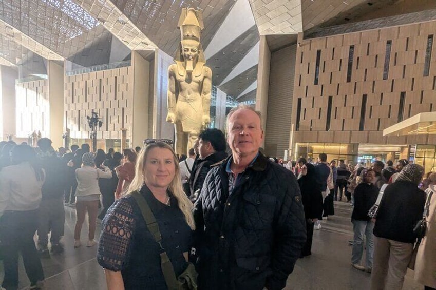 A large golden statue in a modern building with a patterned wall and a crowd of people. 5