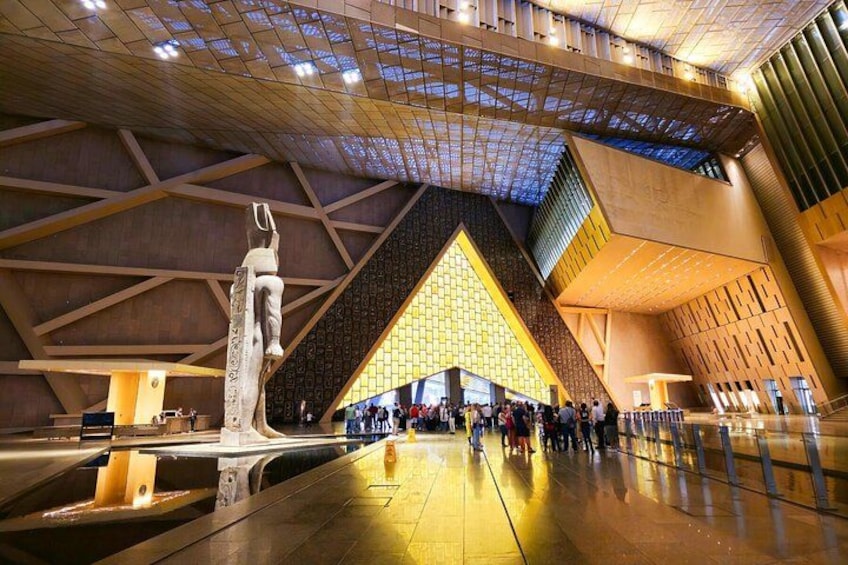 Een modern architecturaal interieur met een grote, driehoekige structuur, een spiegelende vloer en een centraal geplaatst sculptuur. 1