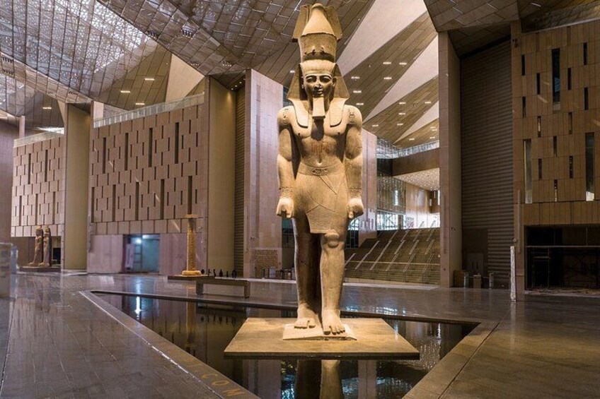 Une grande statue d’un pharaon, placée dans un bâtiment moderne aux murs géométriques et au sol réfléchissant. 2
