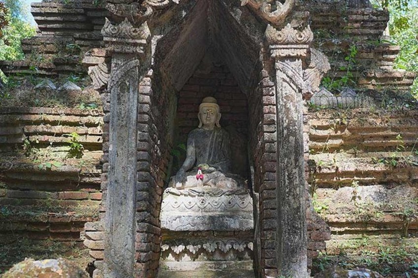 A stone Buddha statue in a niche with intricate carvings, surrounded by weathered brick structures. 4