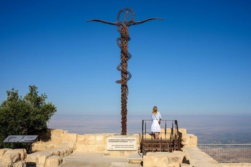 Een hoge metalen sculptuur met een rond bovenstuk, een persoon die op een platform staat, en een helderblauwe lucht. 2
