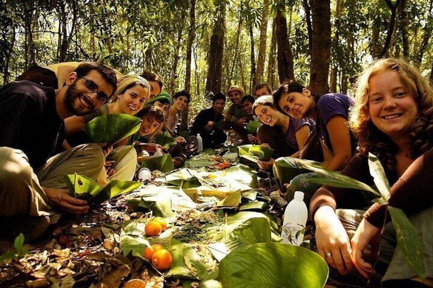 A group of people sitting on the forest floor, surrounded by large leaves and orange fruits. 3