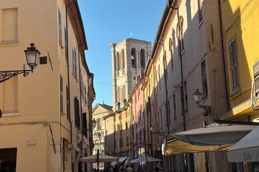 Une rue étroite bordée d’immeubles, avec un clocher d’église et des tables installées à l’extérieur. 3