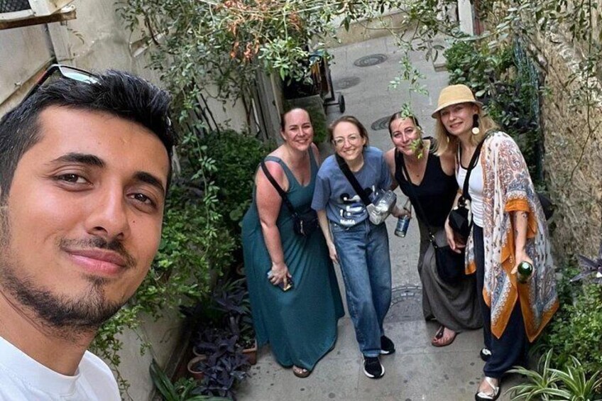 Eine Gruppe von Menschen steht in einer schmalen Gasse, flankiert von Grünpflanzen. 1