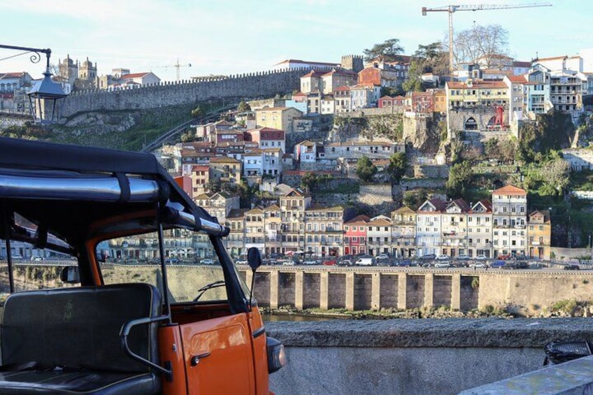 A red vehicle parked on a bridge overlooking a historic town with colorful buildings and a stone wall. 2