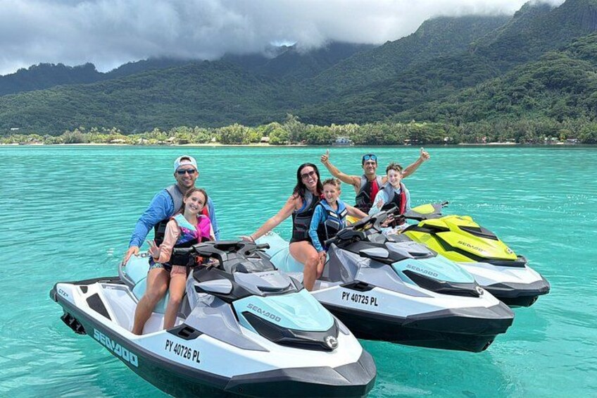 A group of people on jet skis on turquoise water with mountains in the background. 1