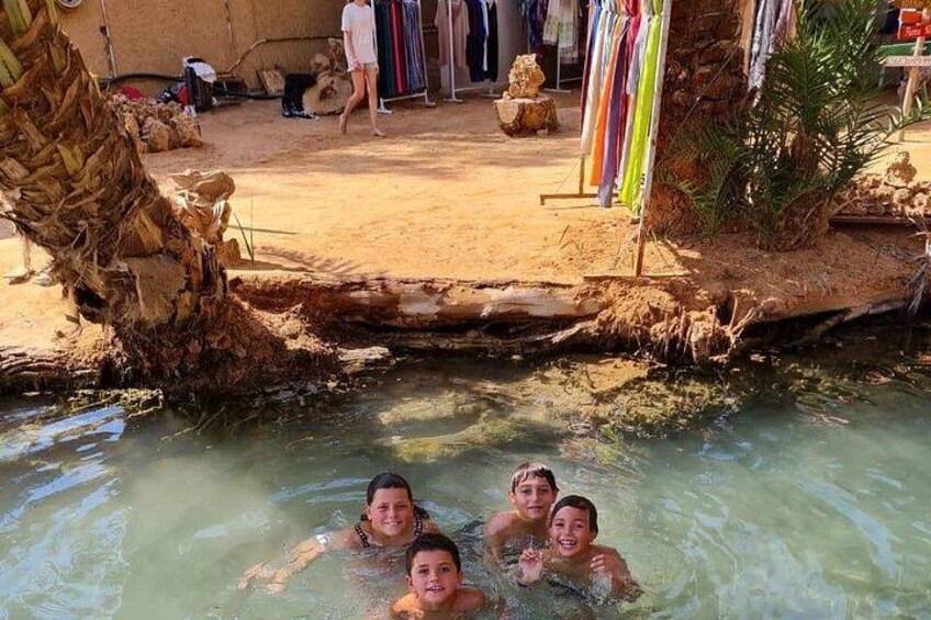 Un grupo de personas en una poza natural, con un tronco de árbol y un tendedero al fondo. 2