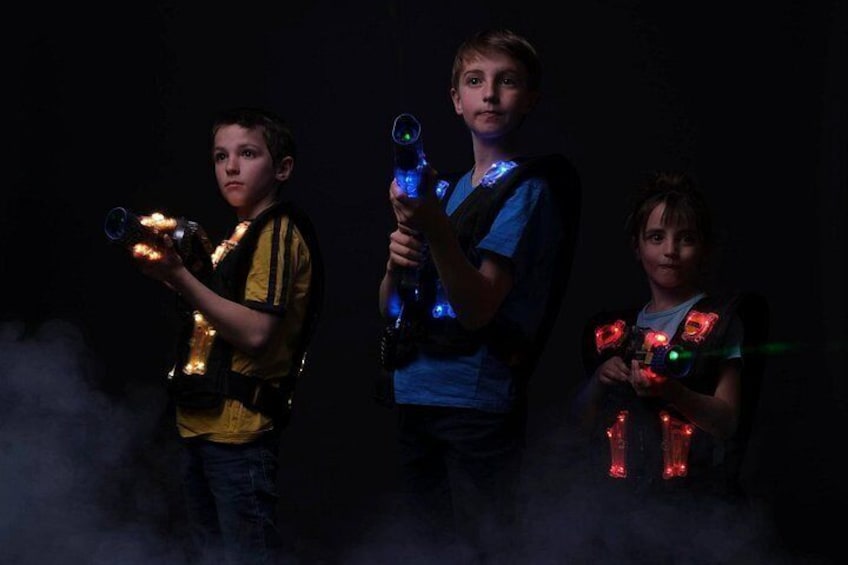 Three children holding glowing devices, possibly for a game or activity, in a dark setting with fog. 1