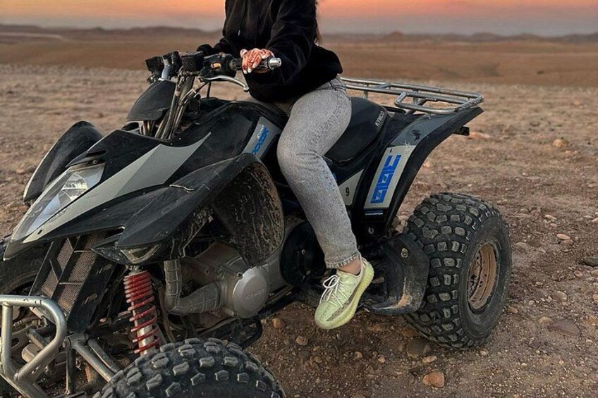 A person sitting on a quad bike in a barren landscape with a sunset in the background. 1