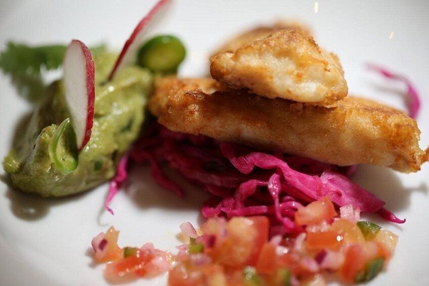 En tallrik med stekt fisk, guacamole, röd kål och en salsasås som garnering. 5