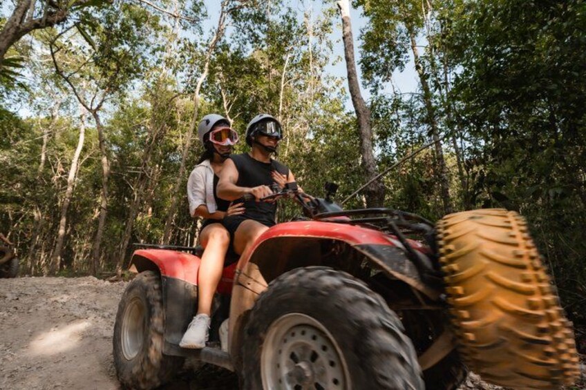 Zwei Personen fahren mit einem roten Quad durch ein bewaldetes Gelände. 2