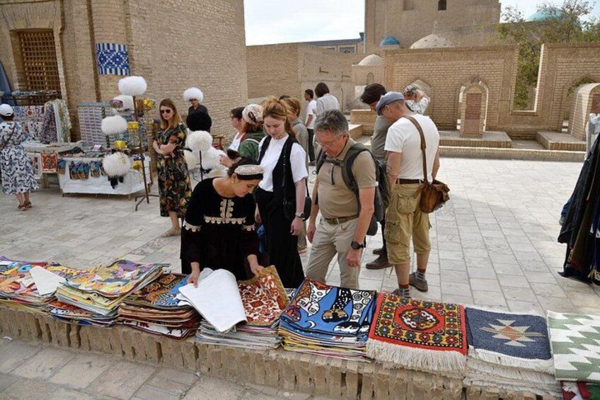 A market scene with people browsing textiles and rugs. 2