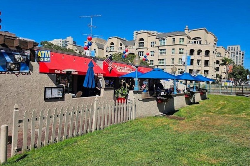 A red ATM kiosk, blue umbrellas, and a white picket fence in a sunny outdoor setting. 5