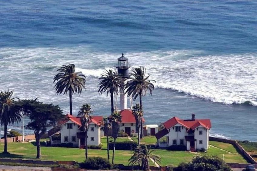 A coastal scene with a lighthouse, palm trees, and white buildings with red roofs. 3