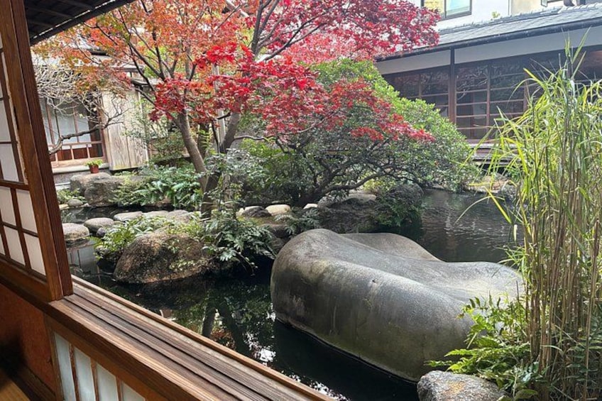 A traditional Japanese garden with a pond, rocks, and a red autumn tree. 3