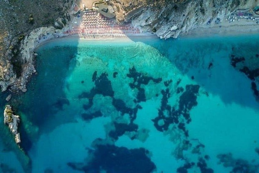A coastal area with clear turquoise waters, a rocky shoreline, and a beach with umbrellas. 5