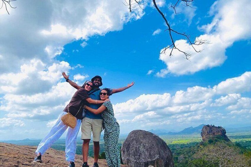 Three people embracing and posing on a hill with a clear sky and distant mountains. 3