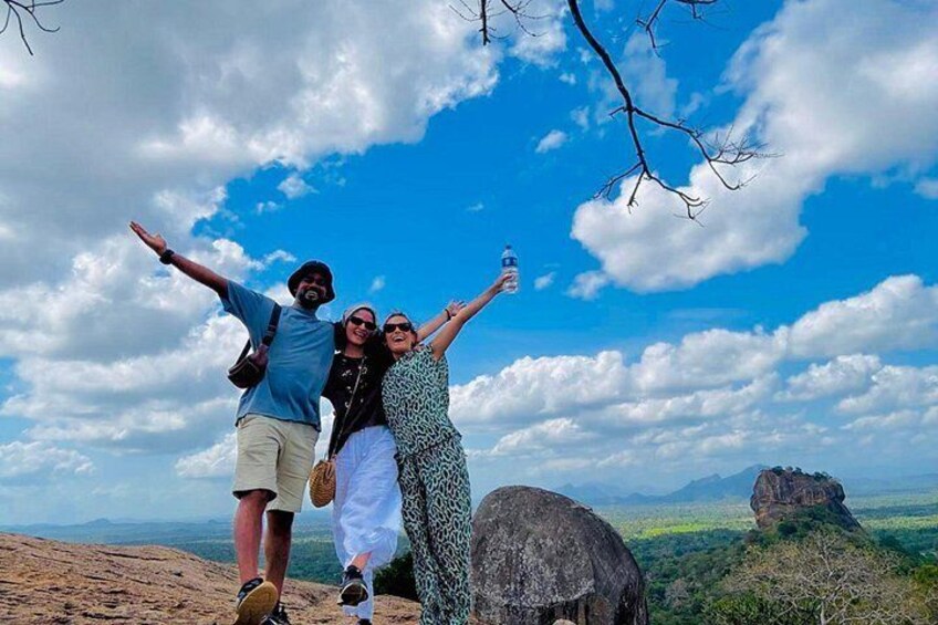 Three people standing on a hill with a clear sky and mountains in the background. 4
