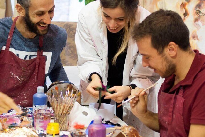 Three people painting at a table with various art supplies. 5