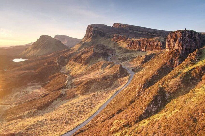 Een ruig berglandschap met een kronkelende weg en een persoon op een klif. 1