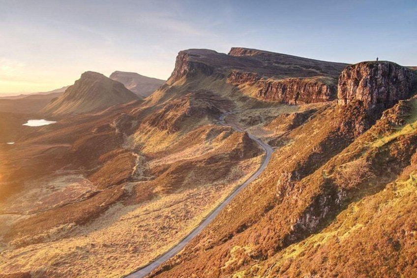 Un paisaje montañoso agreste con un camino sinuoso y una persona de pie en un acantilado. 1
