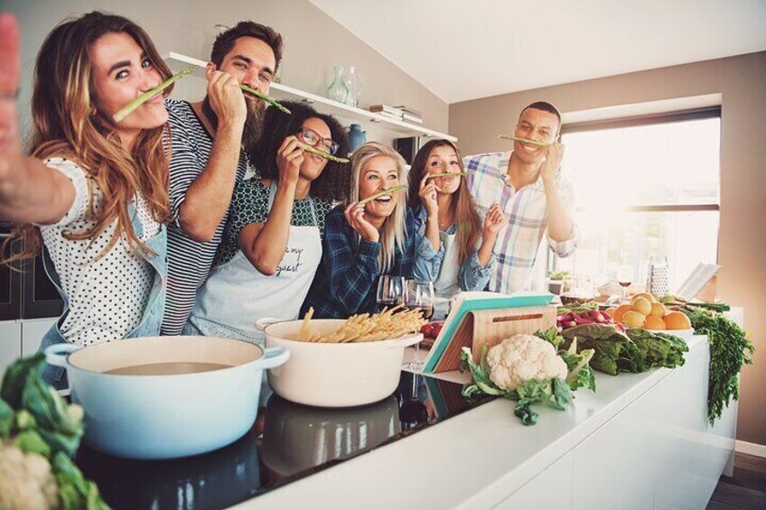 A group of people in a kitchen, some holding chopsticks, with a variety of vegetables and fruits on the counter. 1