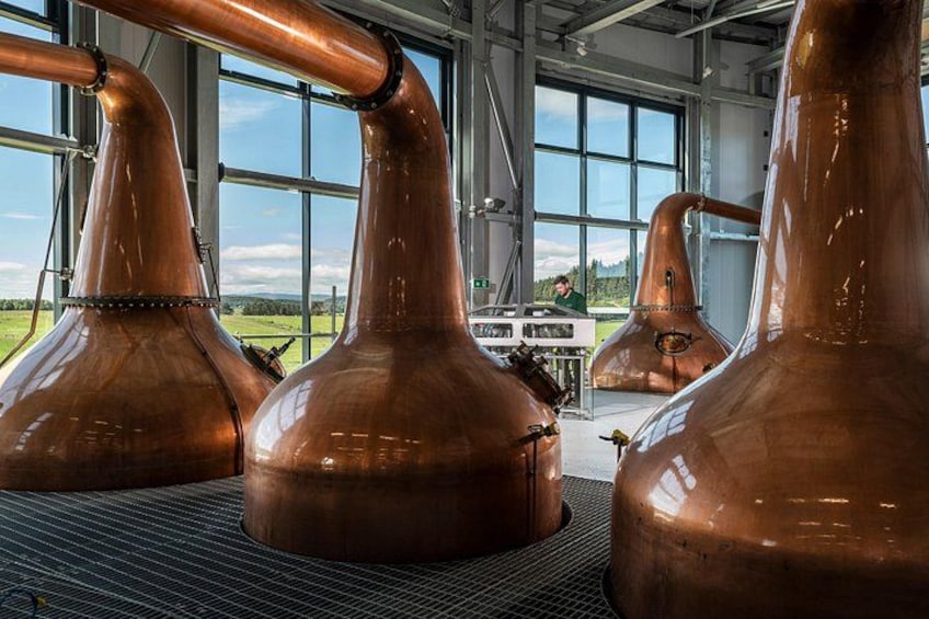 Copper stills in a distillery with large windows and a person in the background. 2