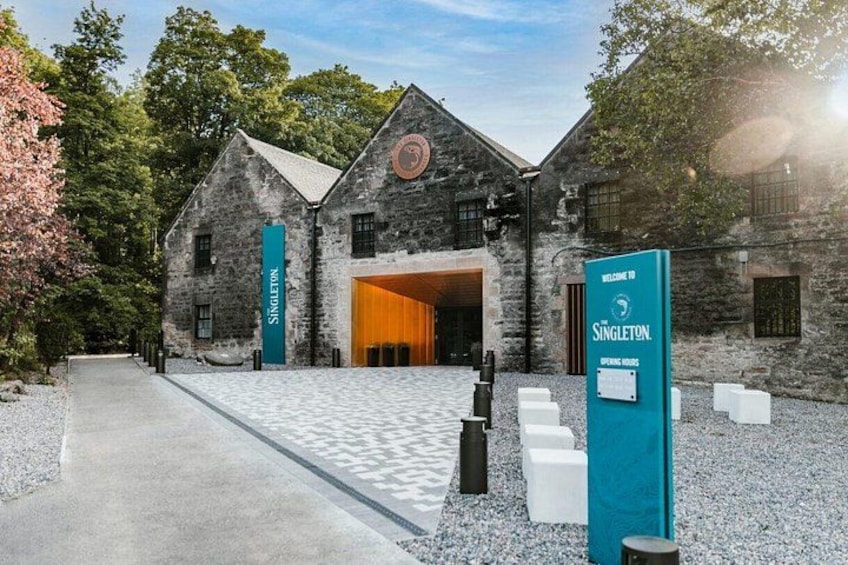 A historic stone building with a large wooden door, surrounded by gravel and trees. 3
