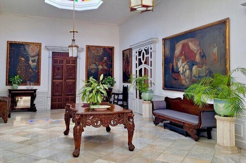 An elegant room with a large wooden table, a sofa, and several paintings on the walls. 1